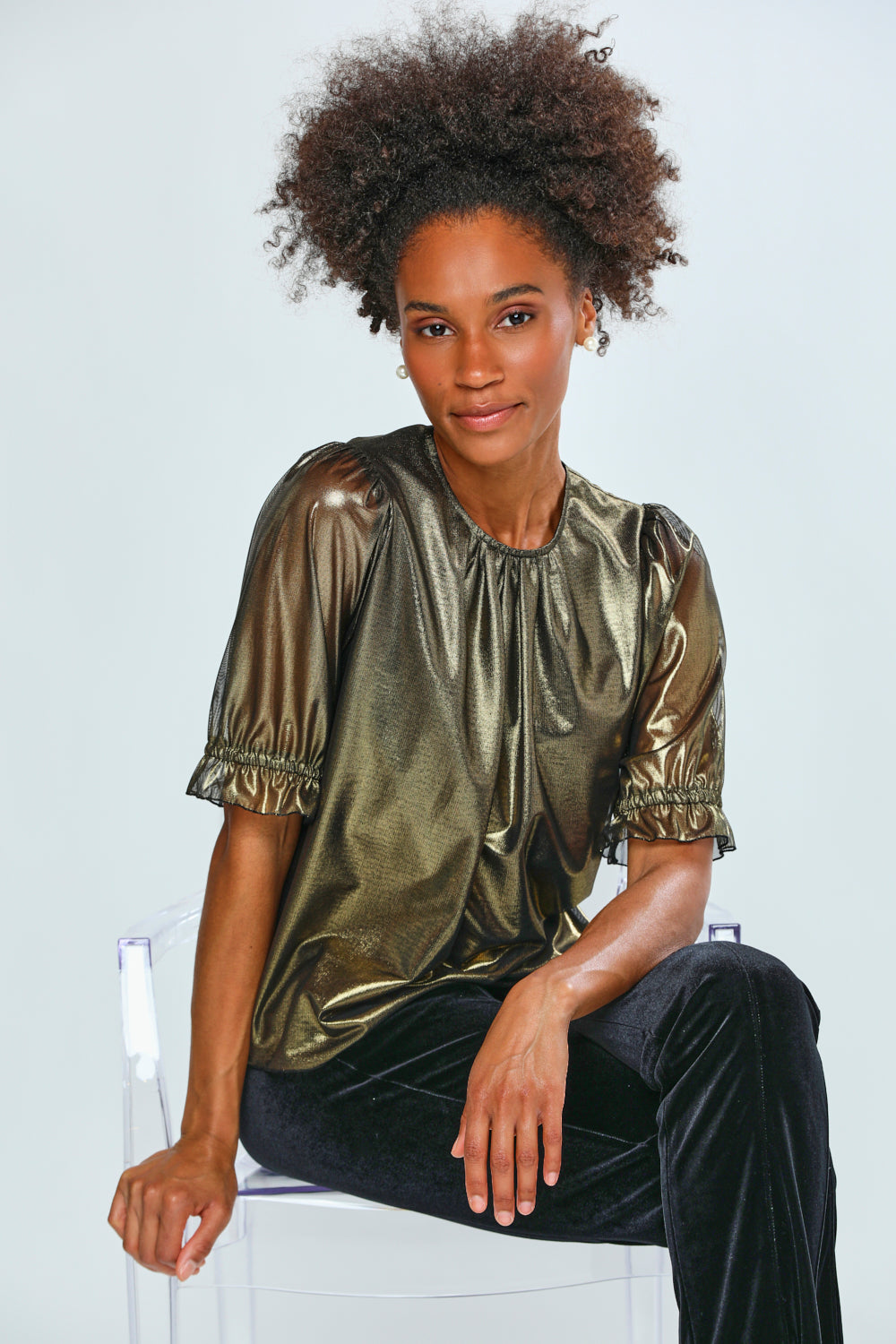 Woman wearing a gold metallic top with black pants on a white background