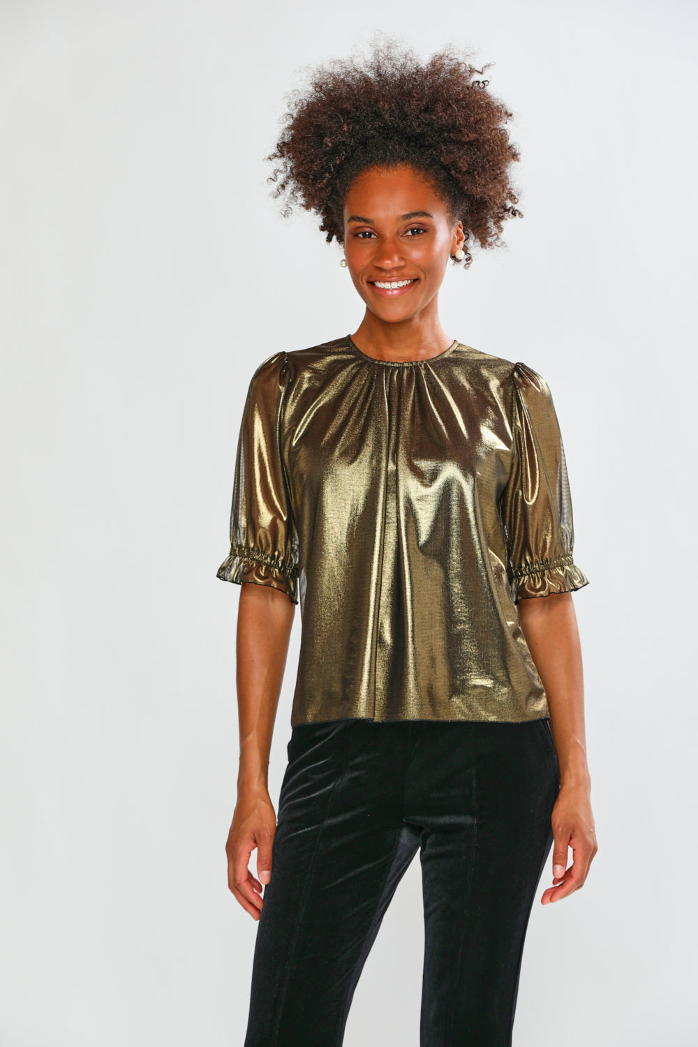 Woman wearing a gold metallic top with black pants on a white background