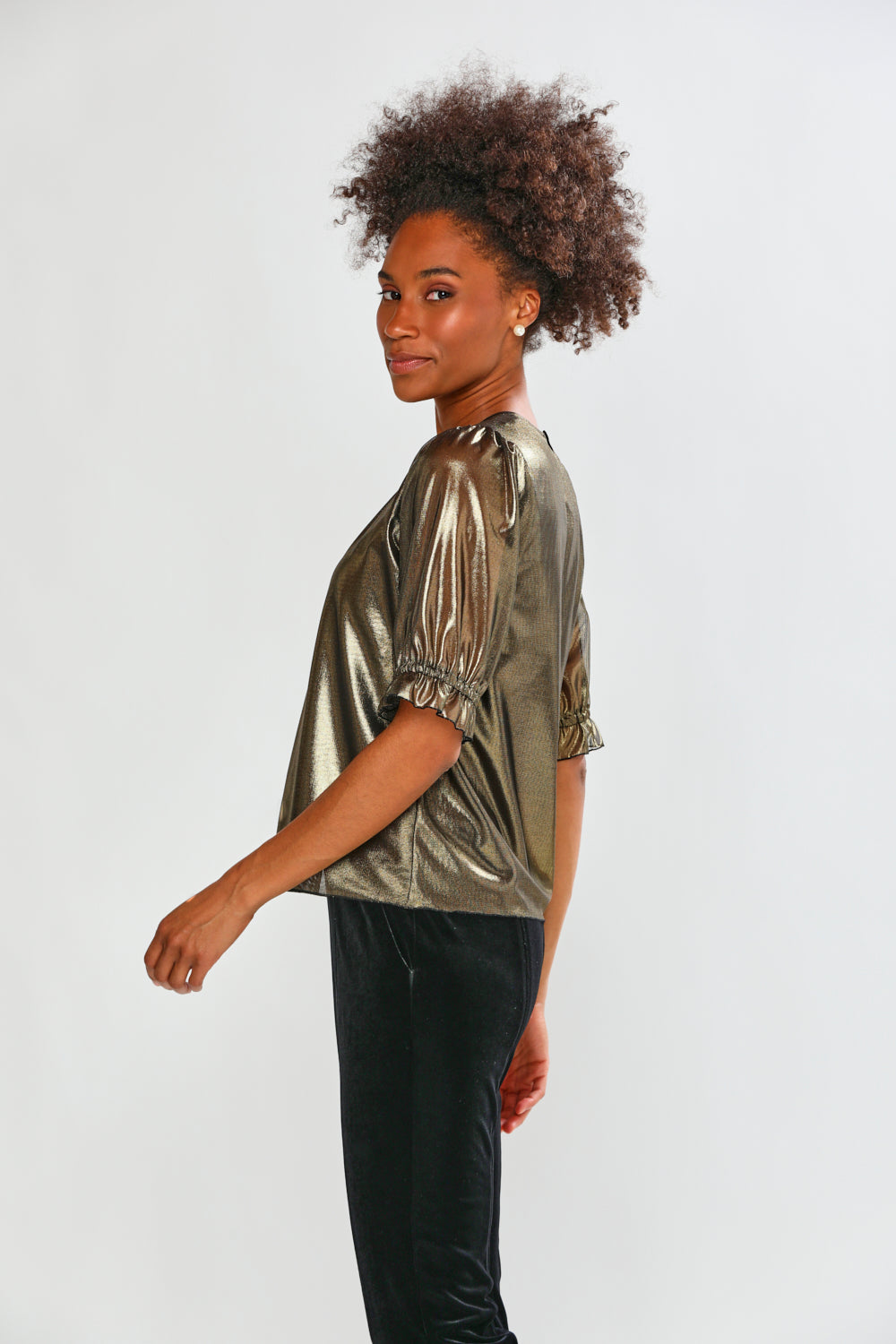 Woman wearing a gold metallic top with black pants on a white background