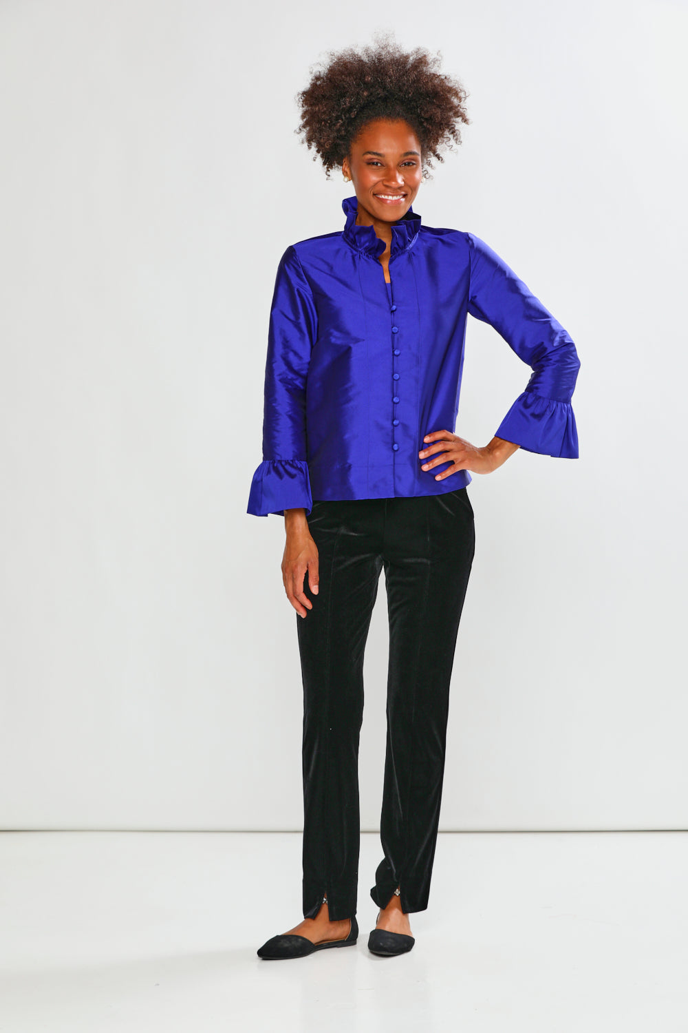 Woman wearing a blue taffeta blouse with black pants on a white background