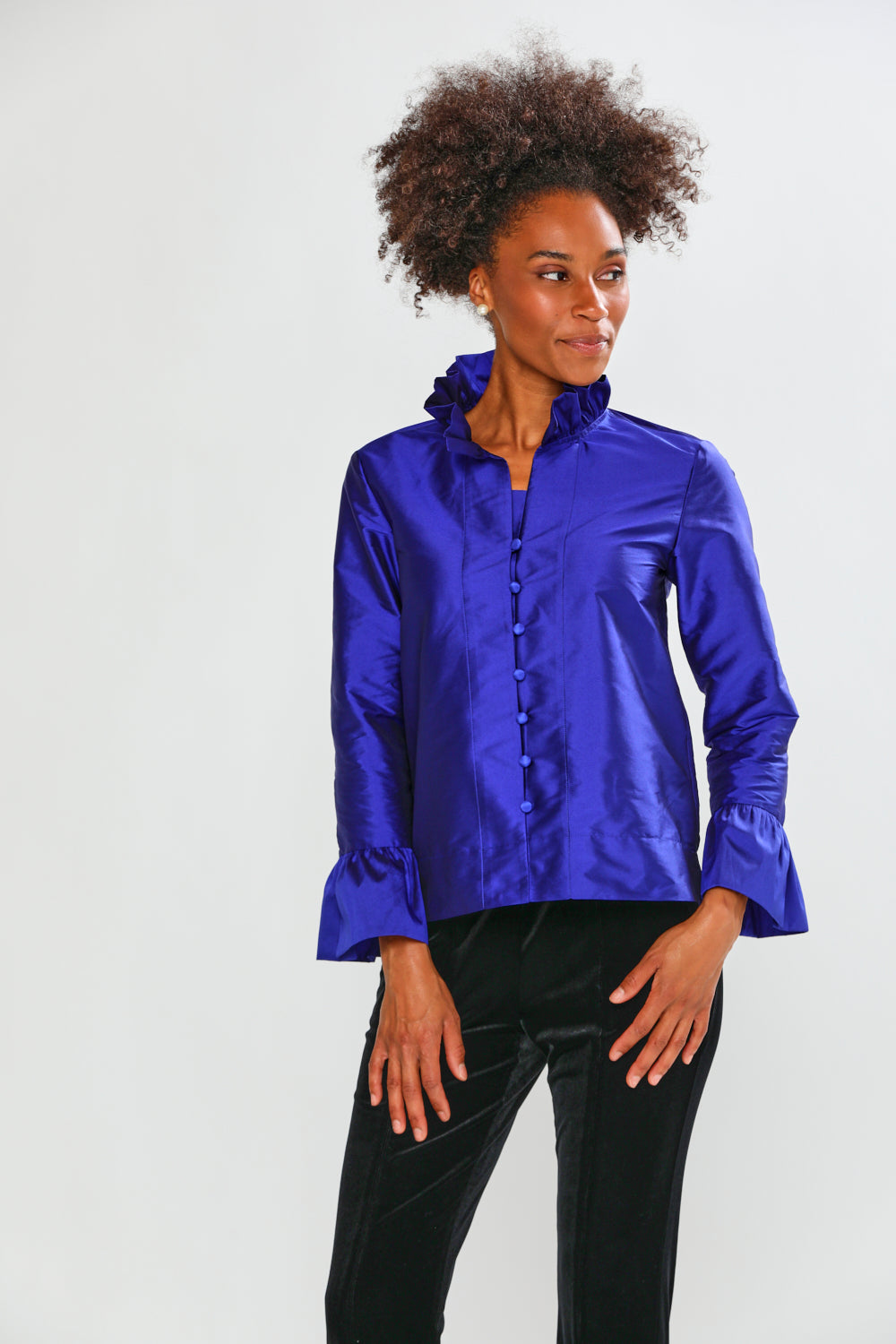 Woman wearing a blue taffeta blouse with black pants on a white background
