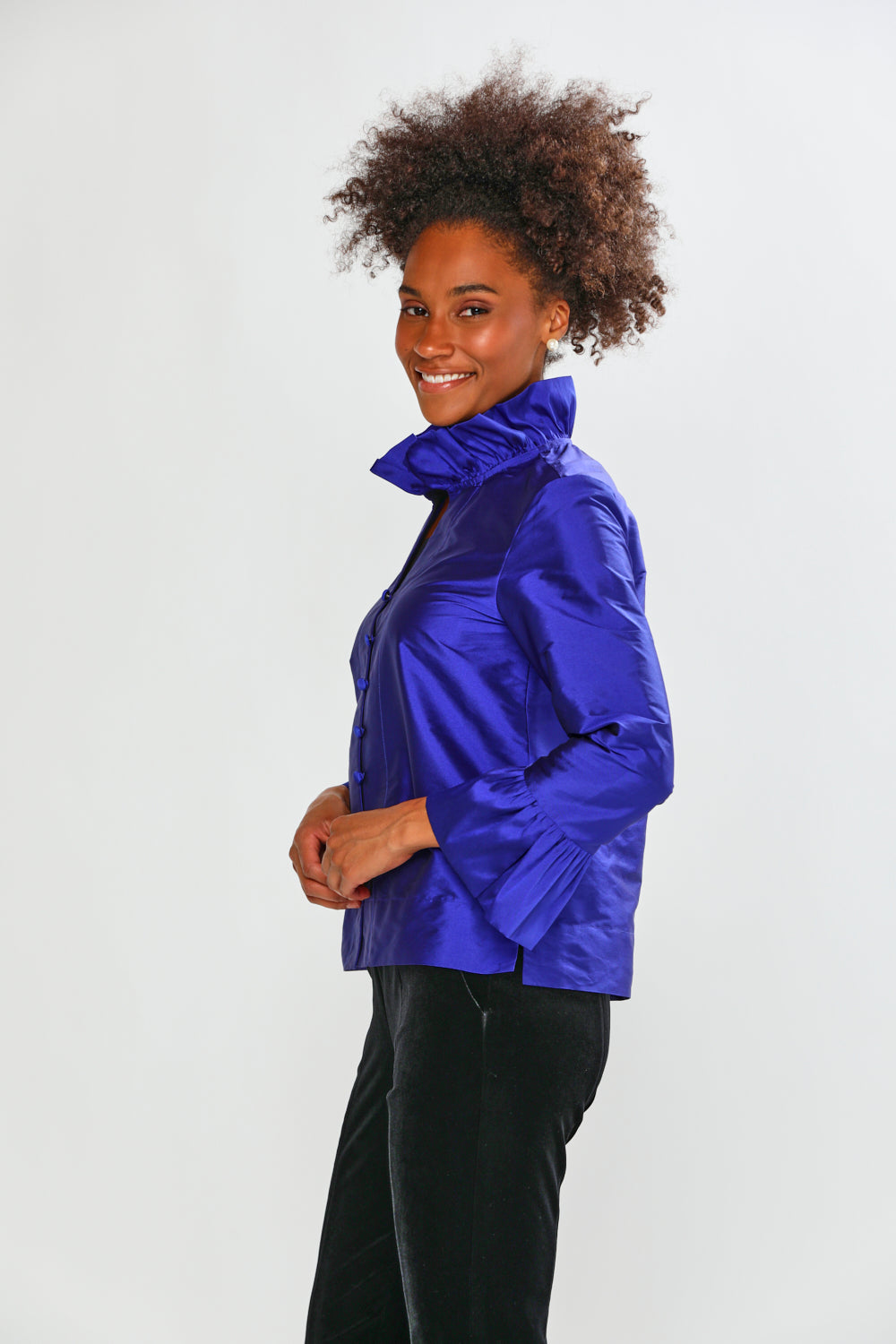 Woman wearing a blue taffeta blouse with black pants on a white background