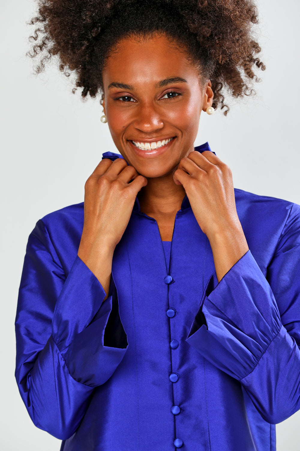Woman wearing a blue taffeta blouse with black pants on a white background