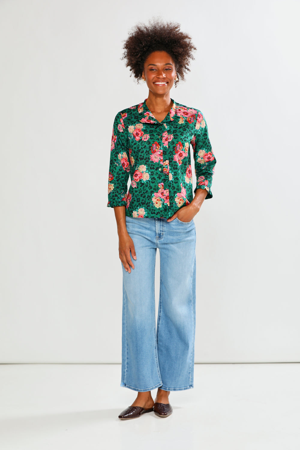 Woman wearing a floral blouse and light blue jeans against a white background