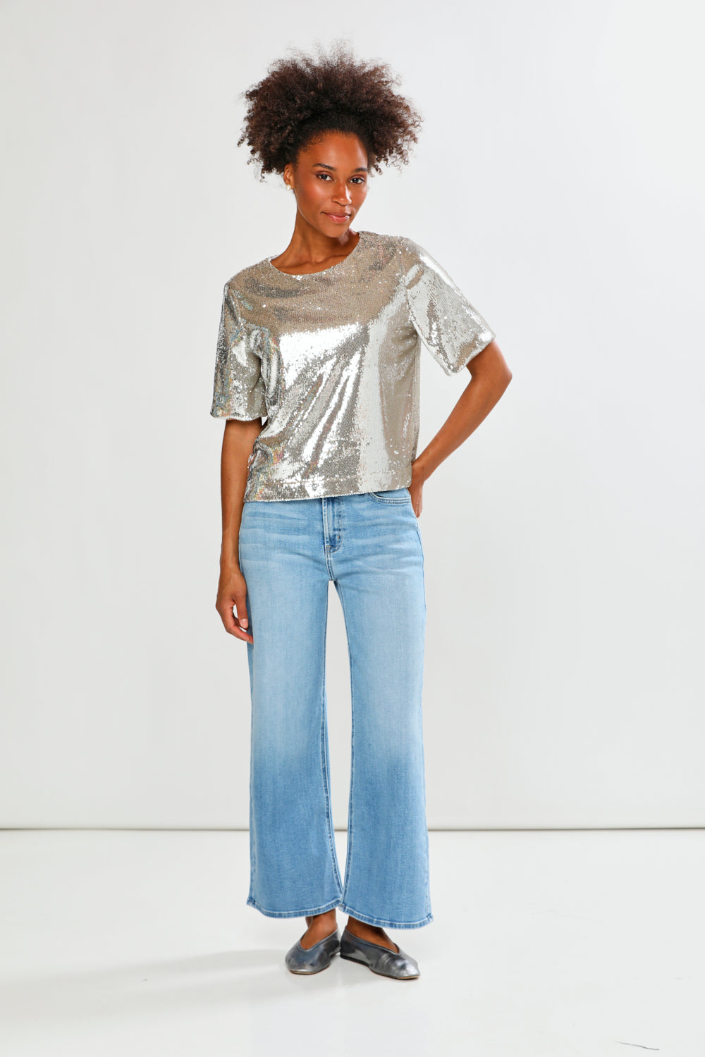 Woman wearing a silver metallic top and light blue jeans on a white background
