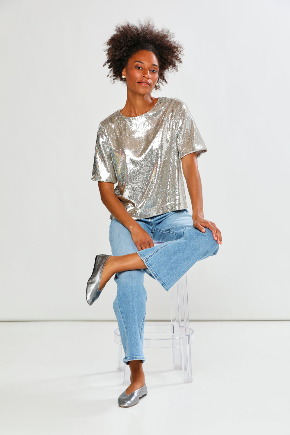 Person wearing a silver sequin top and light blue jeans on a white background