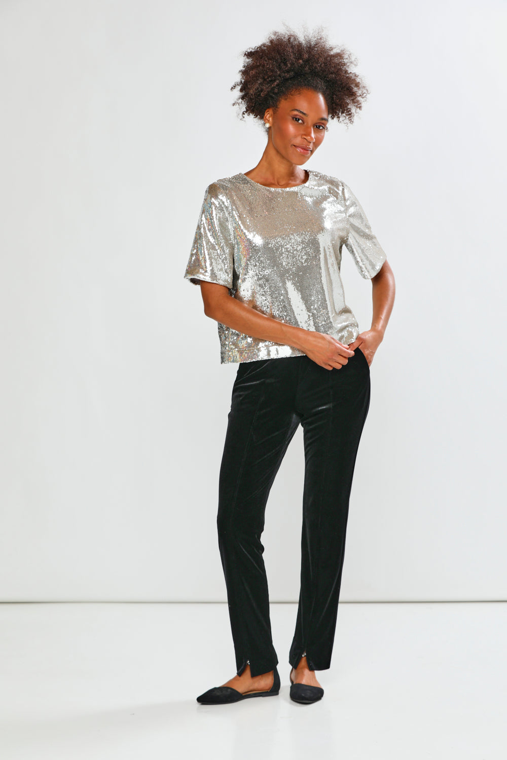 Woman wearing a silver sequin top and black pants on a white background