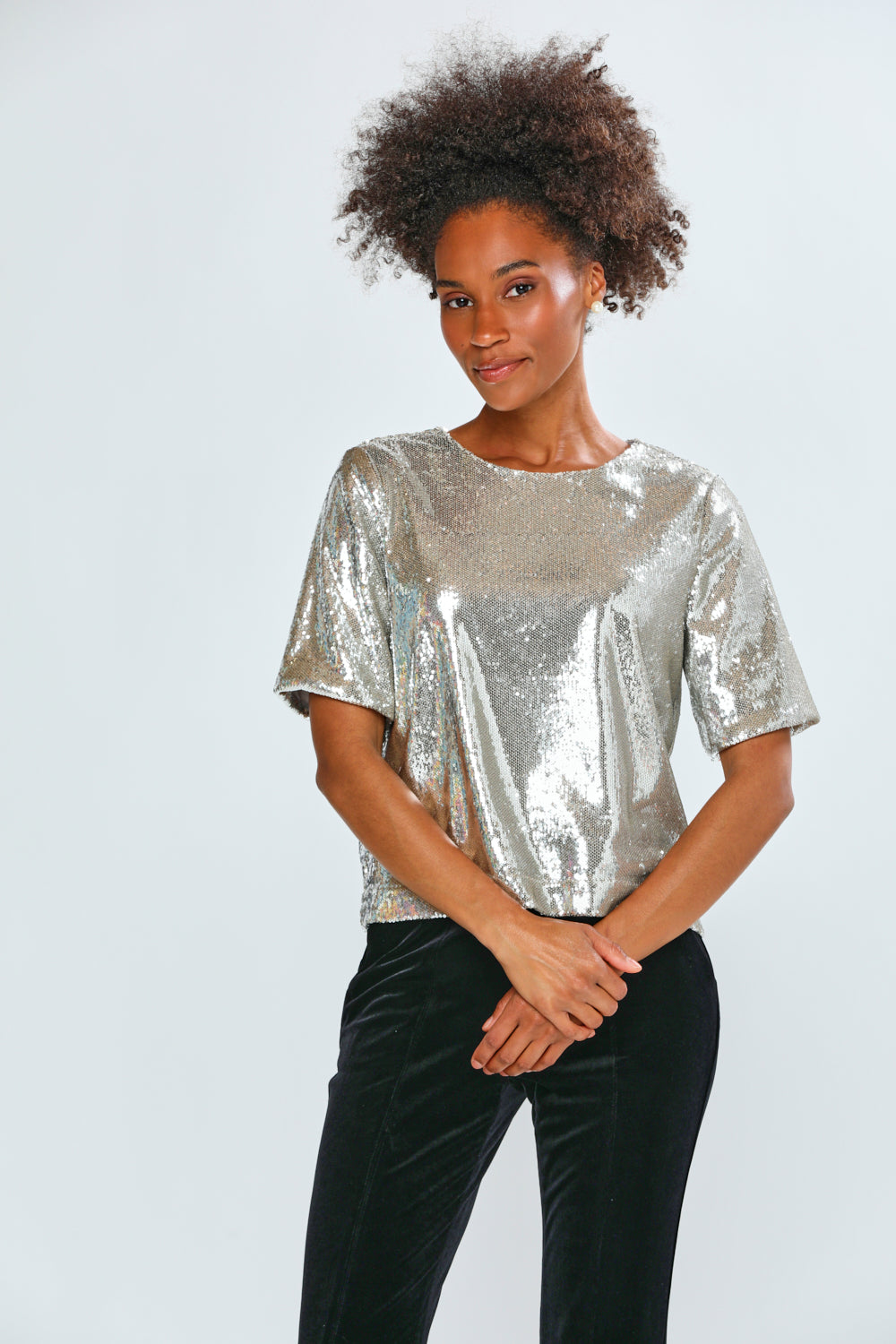 Woman wearing a silver sequin top and black pants on a white background