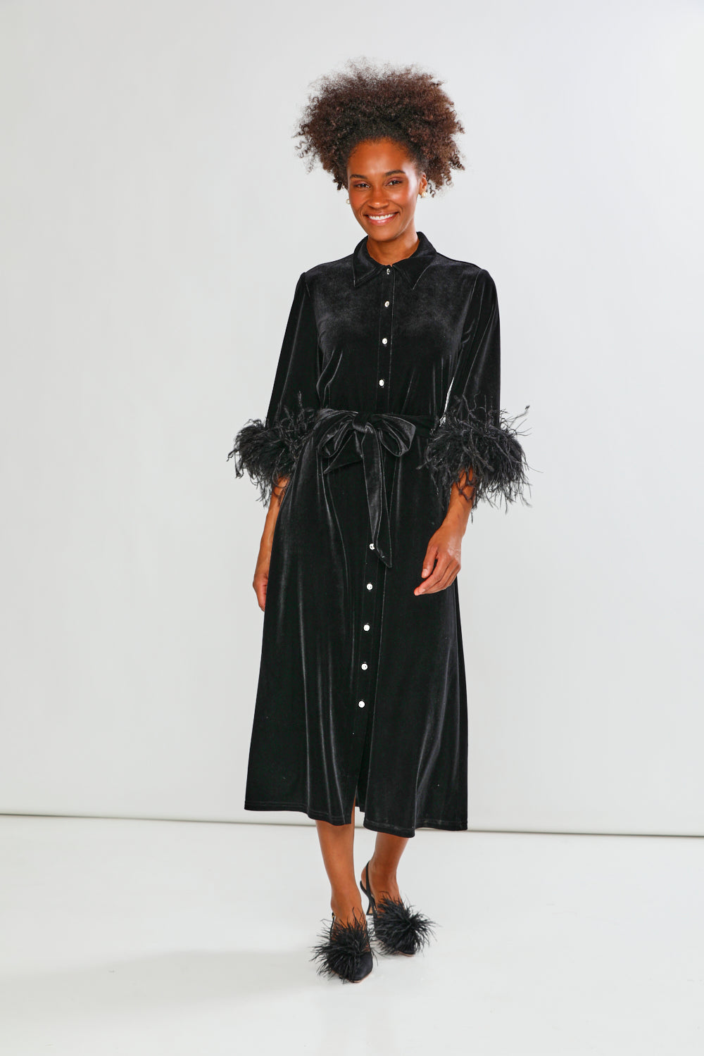Woman wearing a black velvet dress with feathered sleeves on a white background
