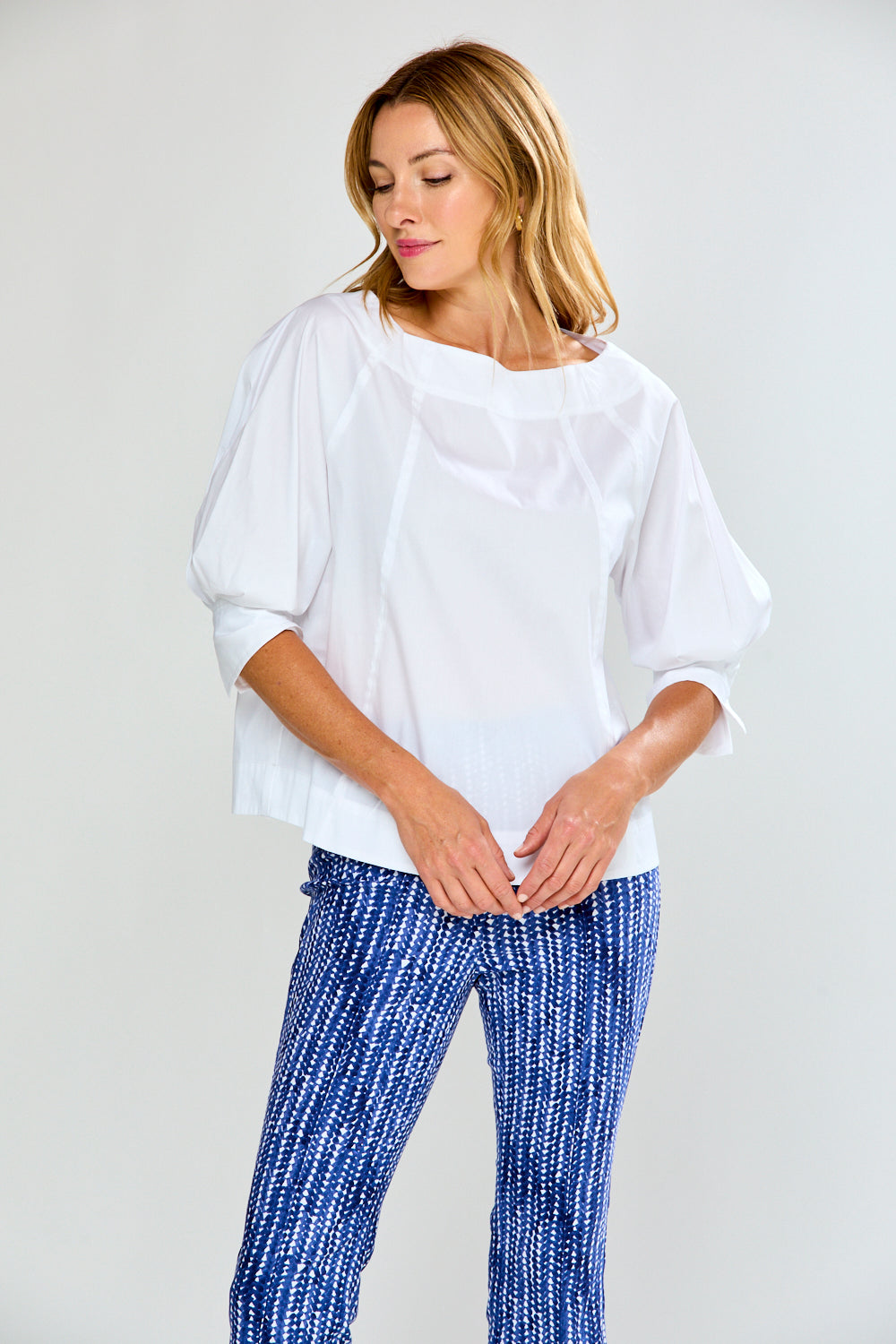 Woman wearing a white blouse and blue patterned pants on a plain background