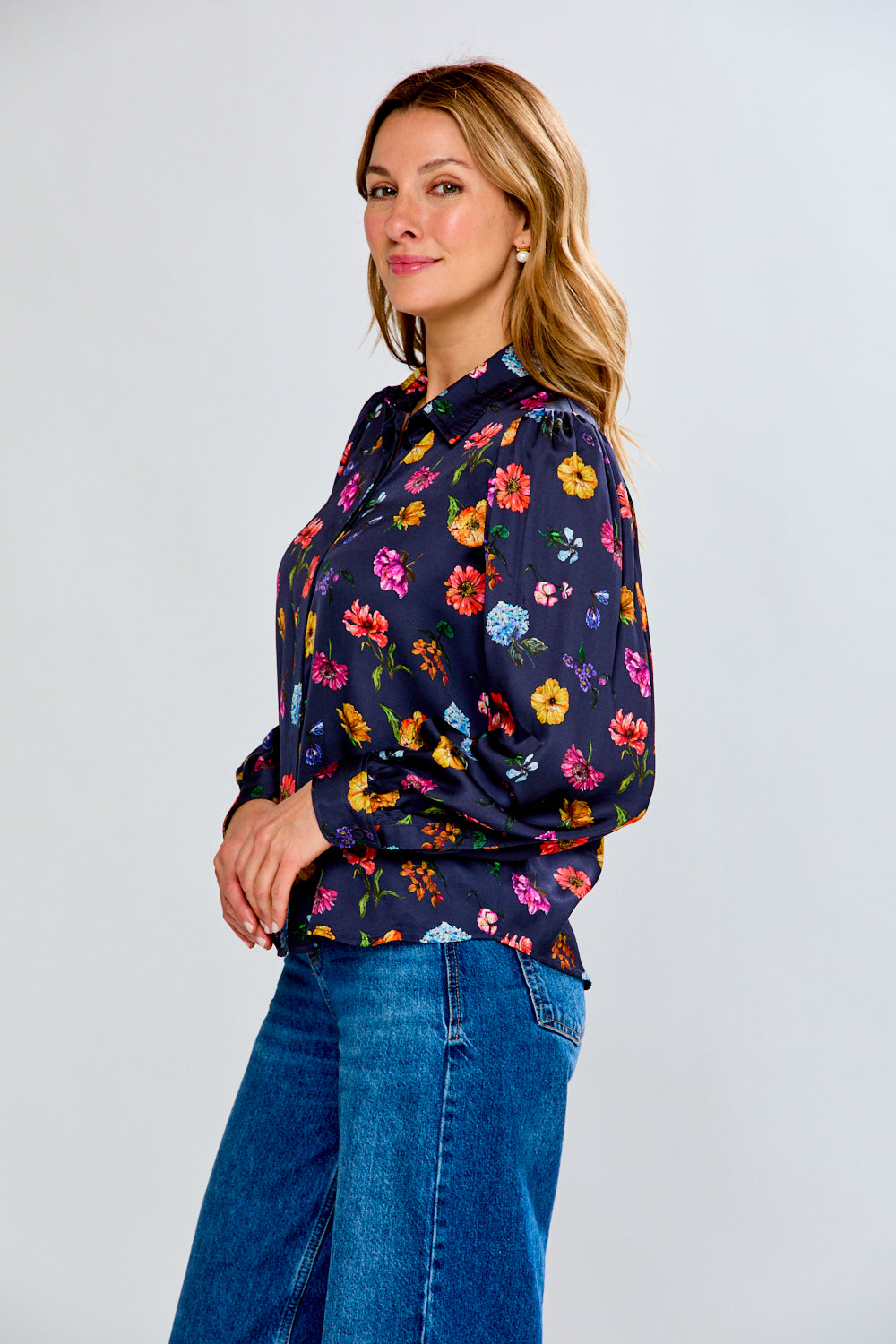 Woman wearing a navy floral blouse and blue jeans on a light gray background