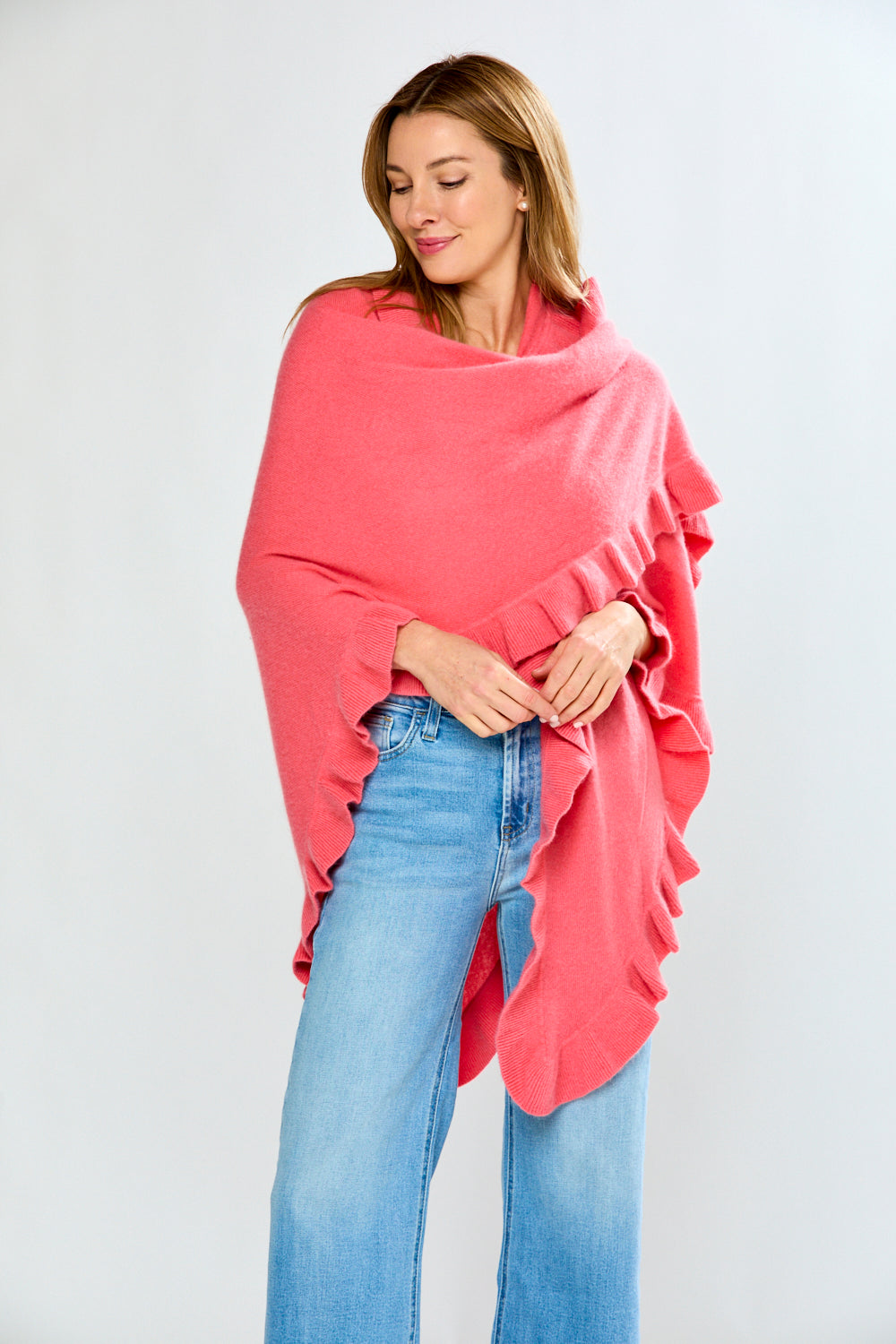 Woman wearing a pink poncho and blue jeans on a white background