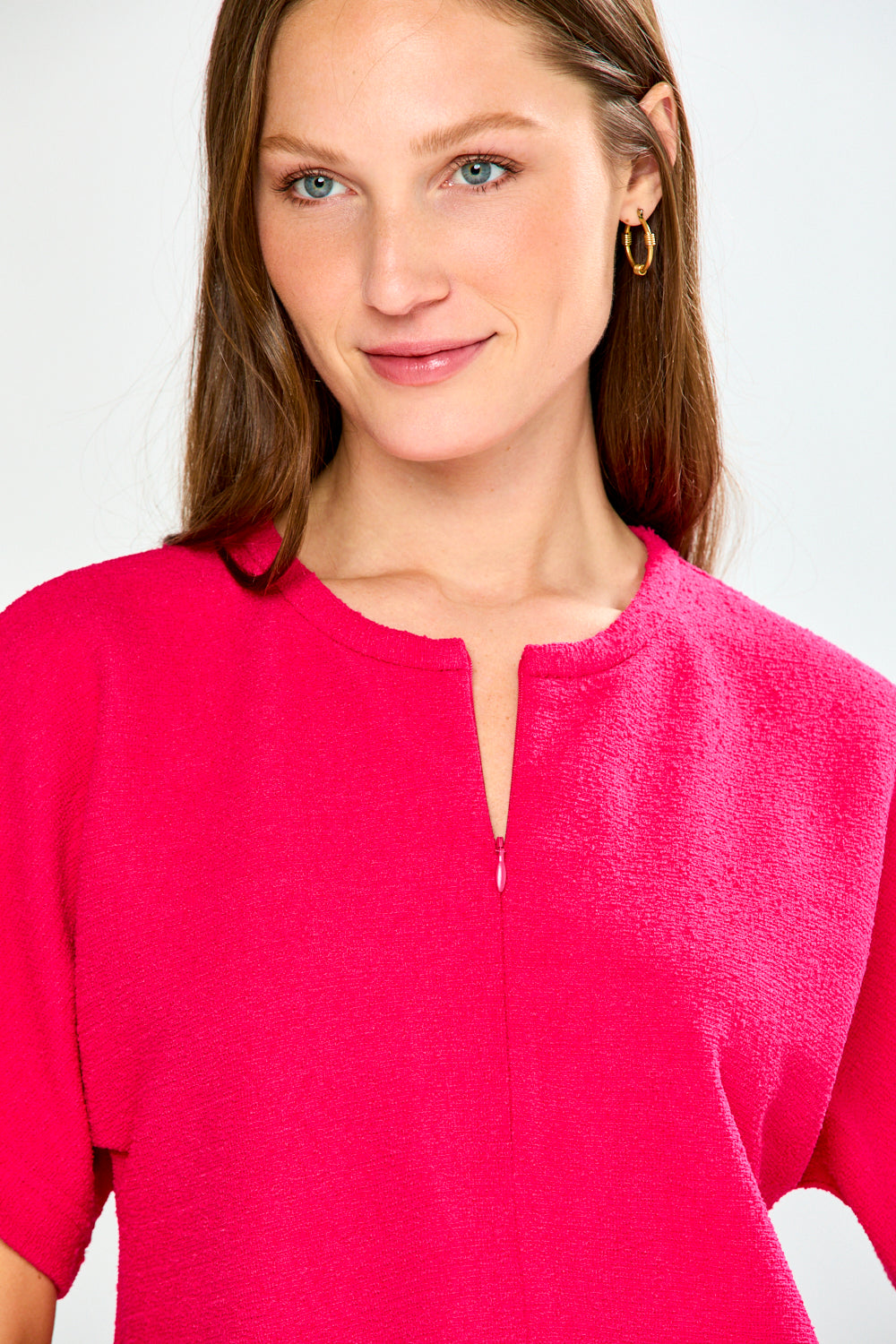 Woman wearing a bright pink top and blue jeans on a white background
