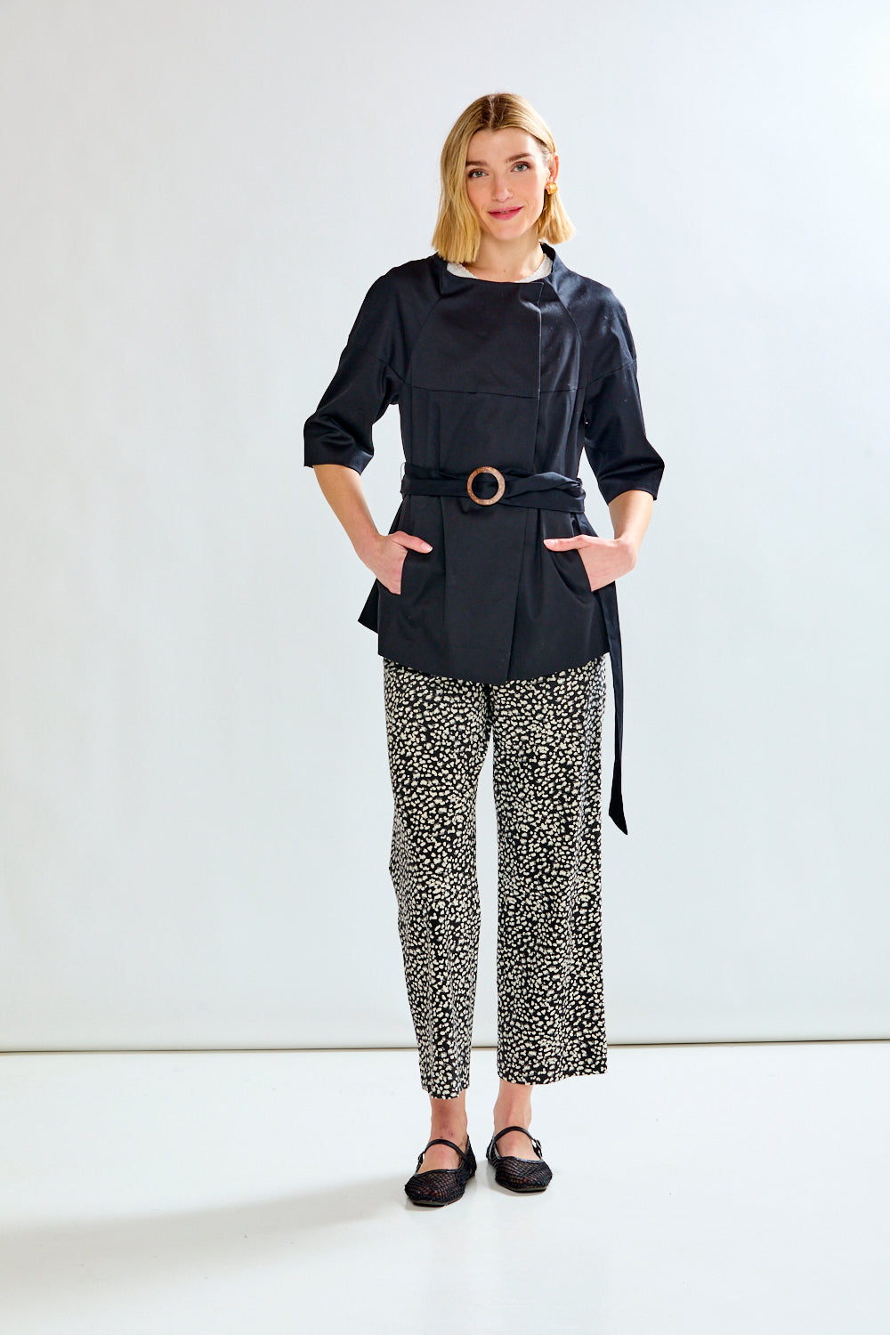 Woman wearing a black belted jacket and patterned pants on a white background