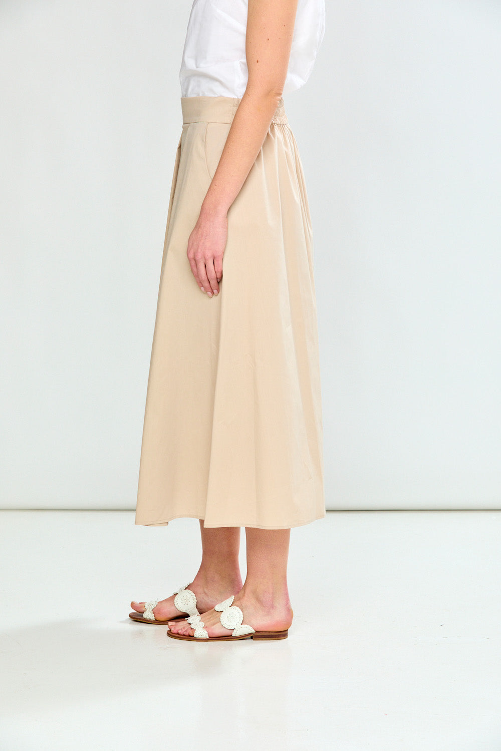 Person wearing a beige skirt and white sandals on a plain background