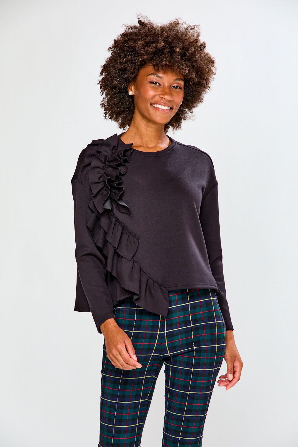 Woman wearing a black ruffled top and plaid pants on a white background