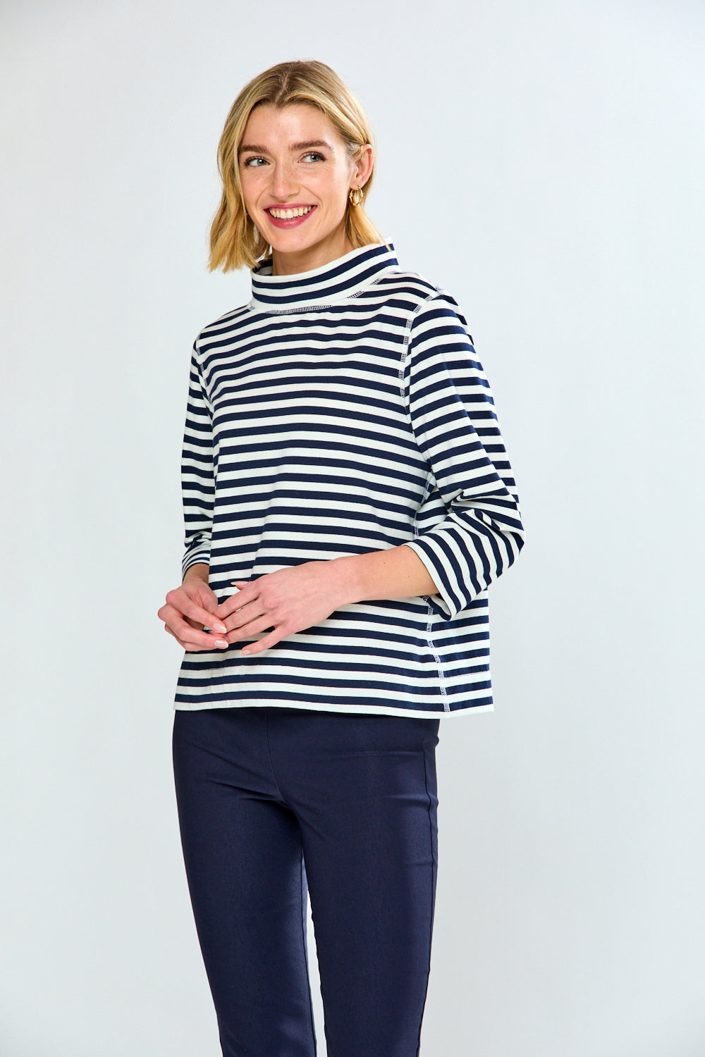 Woman wearing a black and white striped long-sleeve top and navy pants on a light gray background