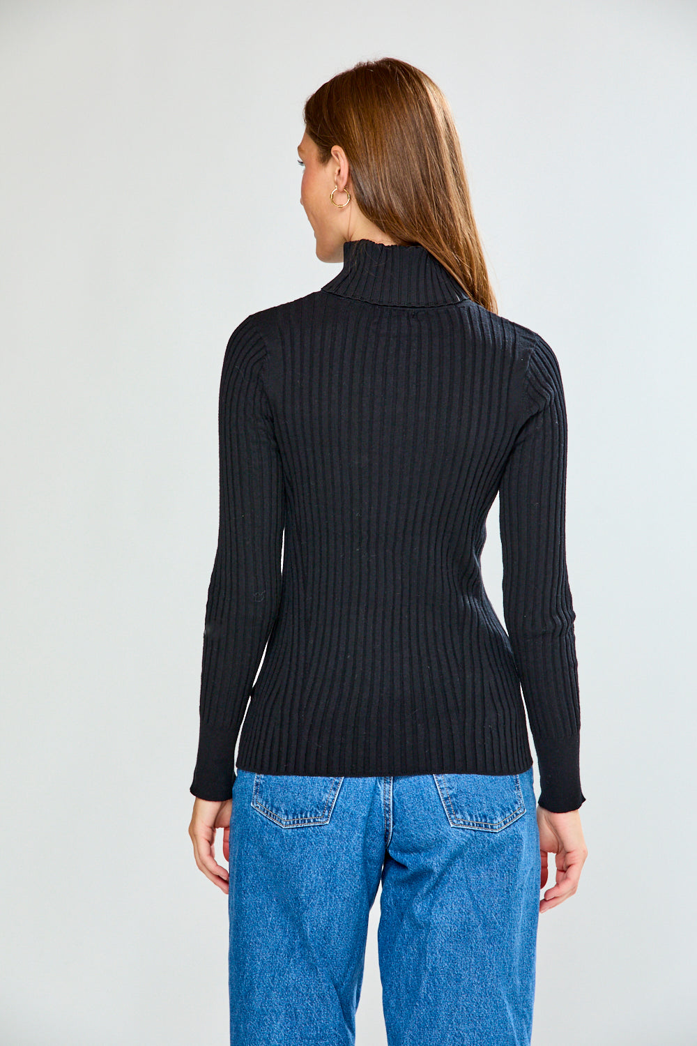 Woman wearing a black ribbed turtleneck sweater and blue jeans on a white background