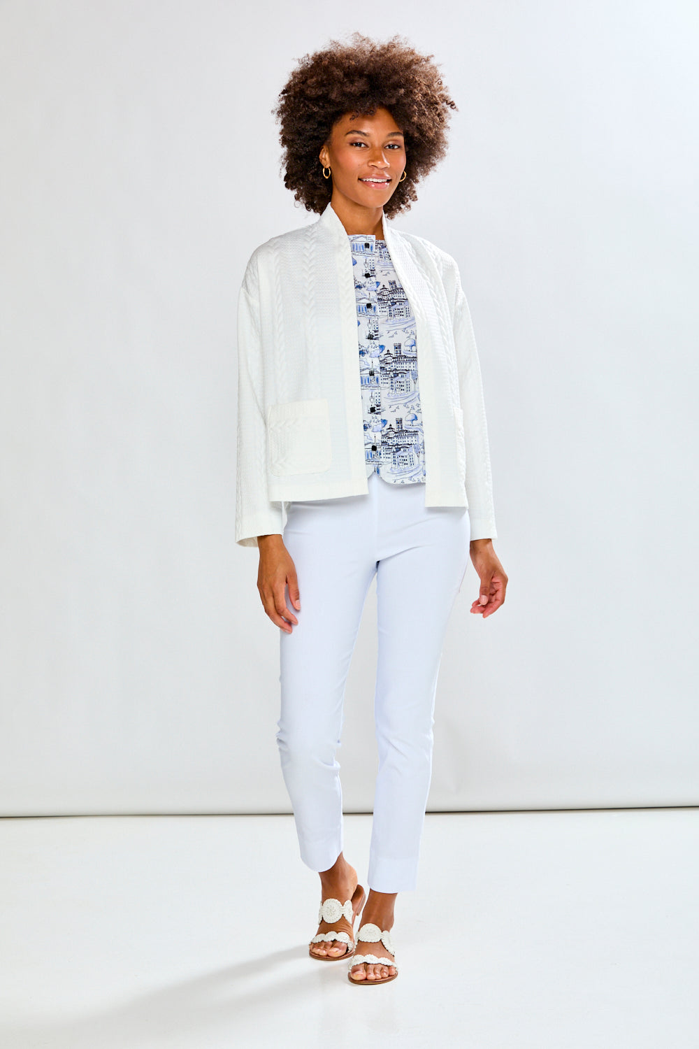 Person wearing a white cardigan and pants against a light gray background