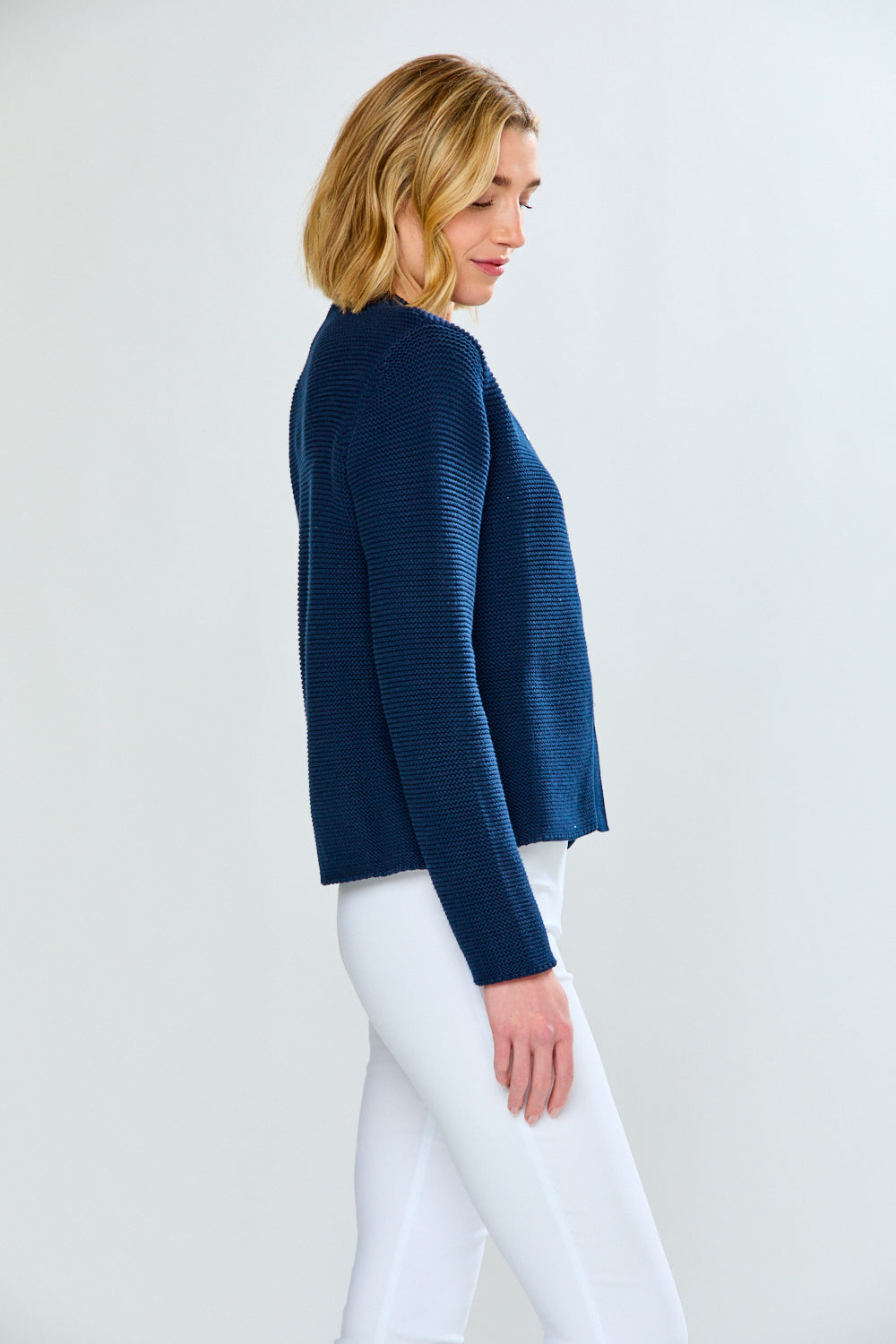 Woman wearing a navy blue sweater and white pants on a light gray background