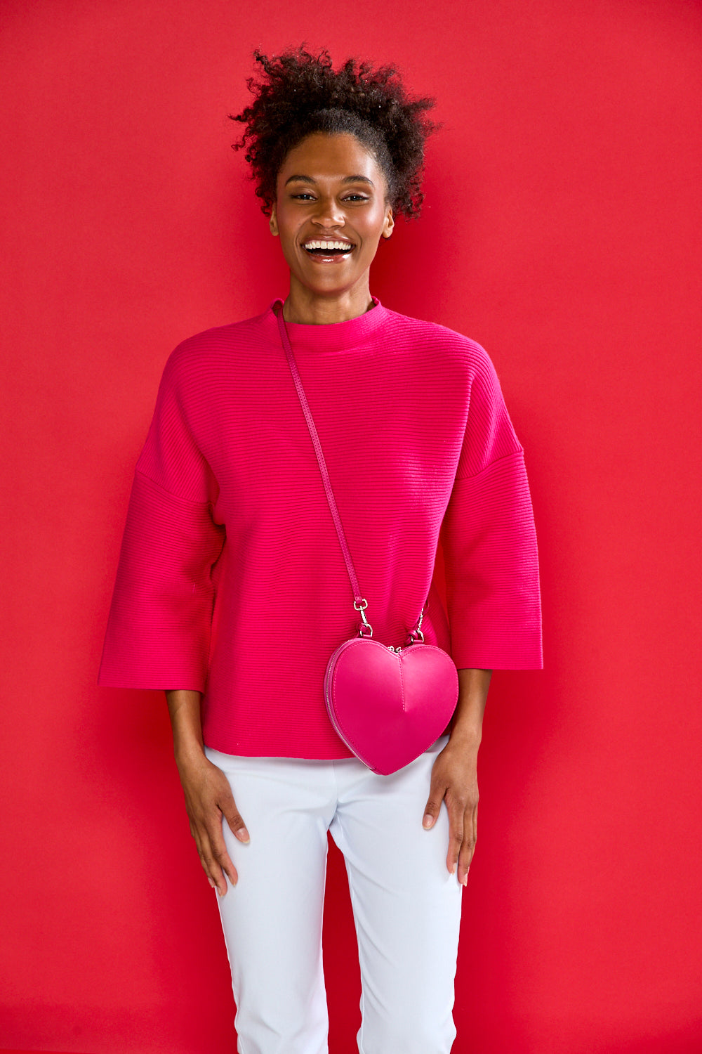 Woman wearing a bright pink outfit with a heart-shaped bag against a red background