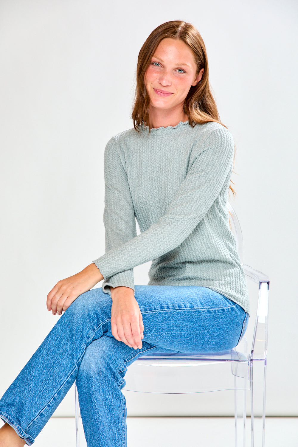 Woman wearing a light grey ribbed shirt and blue jeans on a white background
