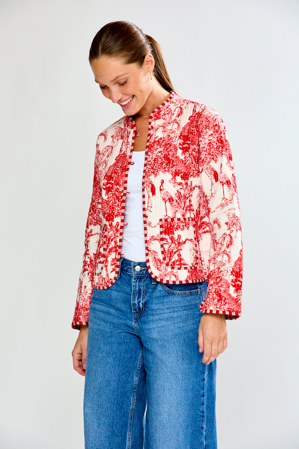 Woman wearing a red and white patterned jacket and blue jeans on a plain background