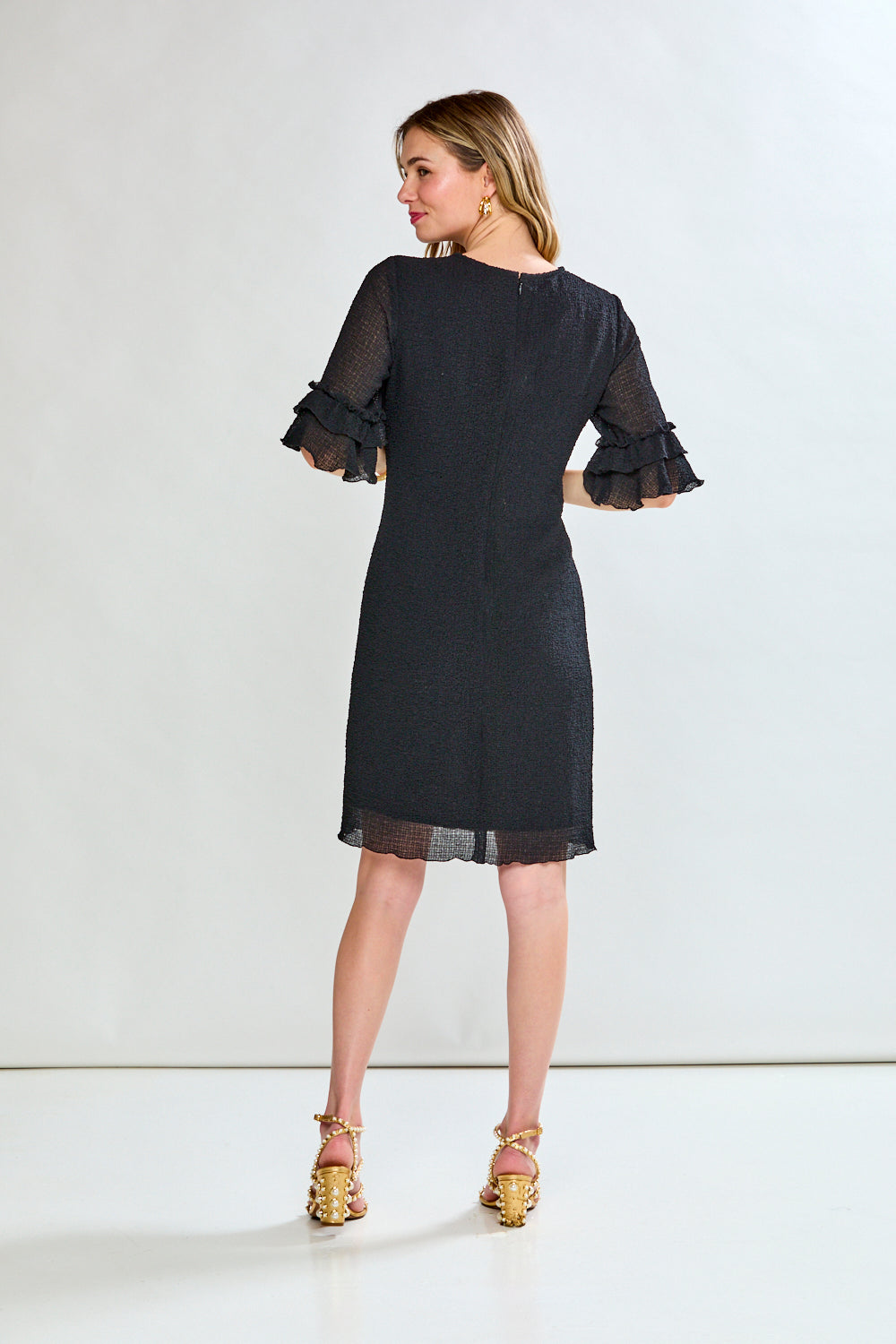 Woman wearing a black dress with sheer sleeves on a white background