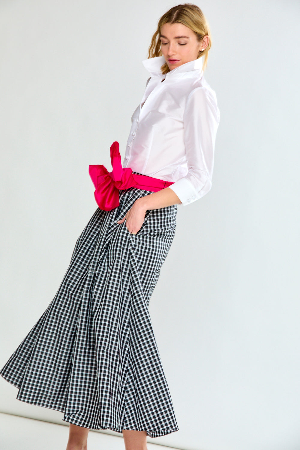 Woman wearing a white blouse with a pink bow and a black and white checkered skirt on a white background