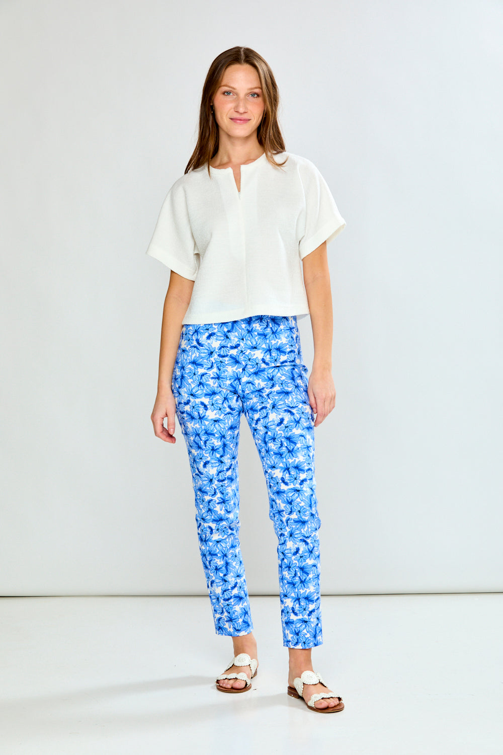 Woman wearing a white top and blue floral pants on a plain background