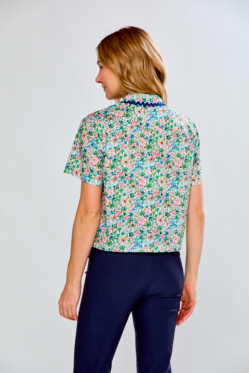 Woman wearing a floral blouse and navy pants on a light gray background