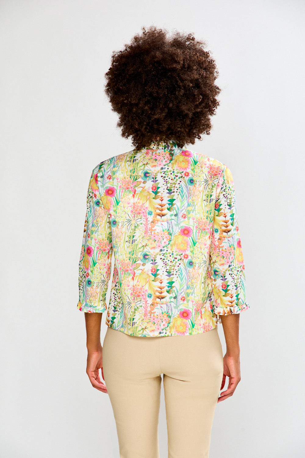 Person wearing a colorful floral blouse with beige pants on a white background