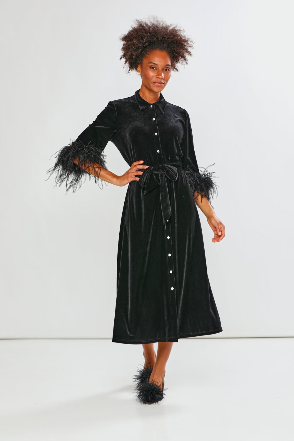 Woman wearing a black velvet dress with feathered sleeves on a white background