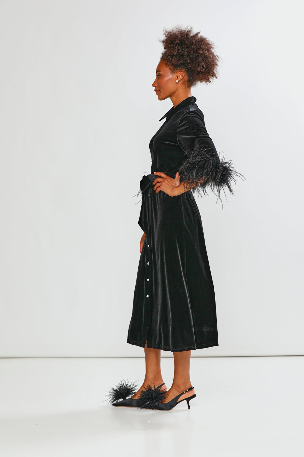 Woman wearing a black velvet dress with feathered sleeves on a white background