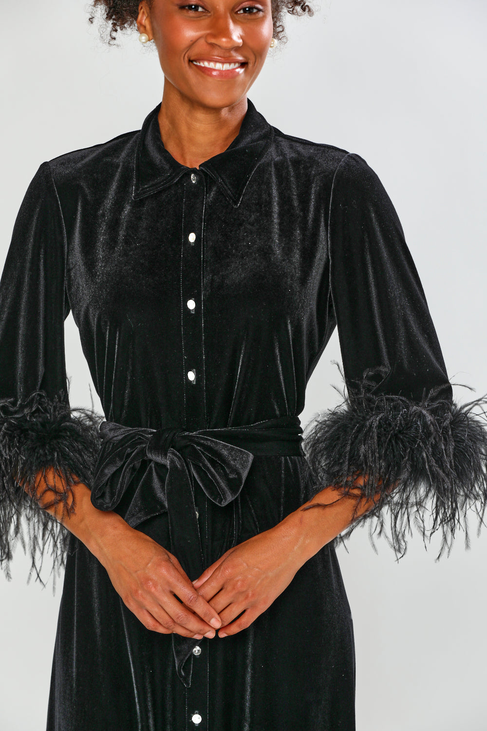 Woman wearing a black velvet dress with feathered sleeves on a white background