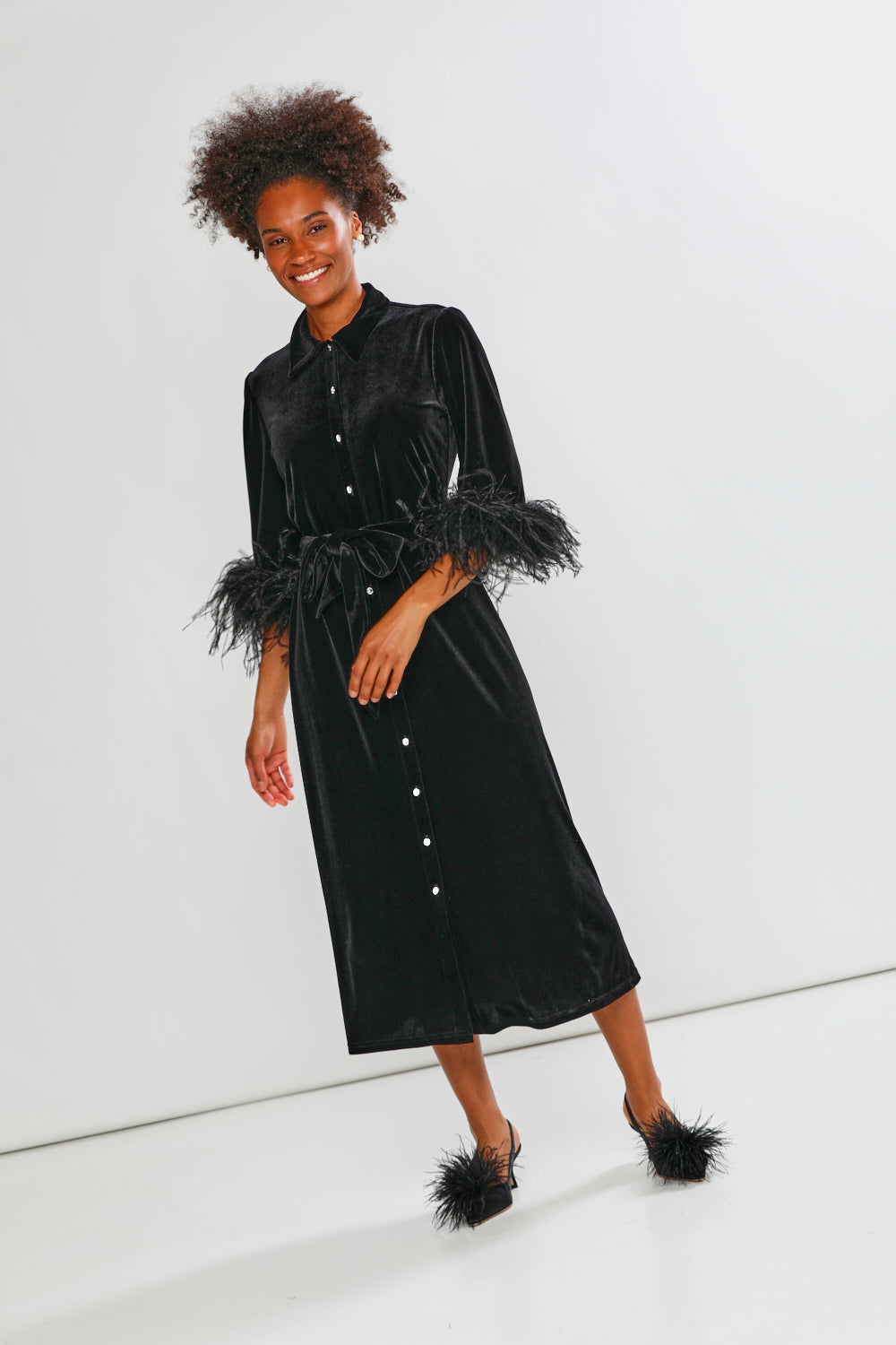 Woman wearing a black velvet dress with feathered sleeves on a white background
