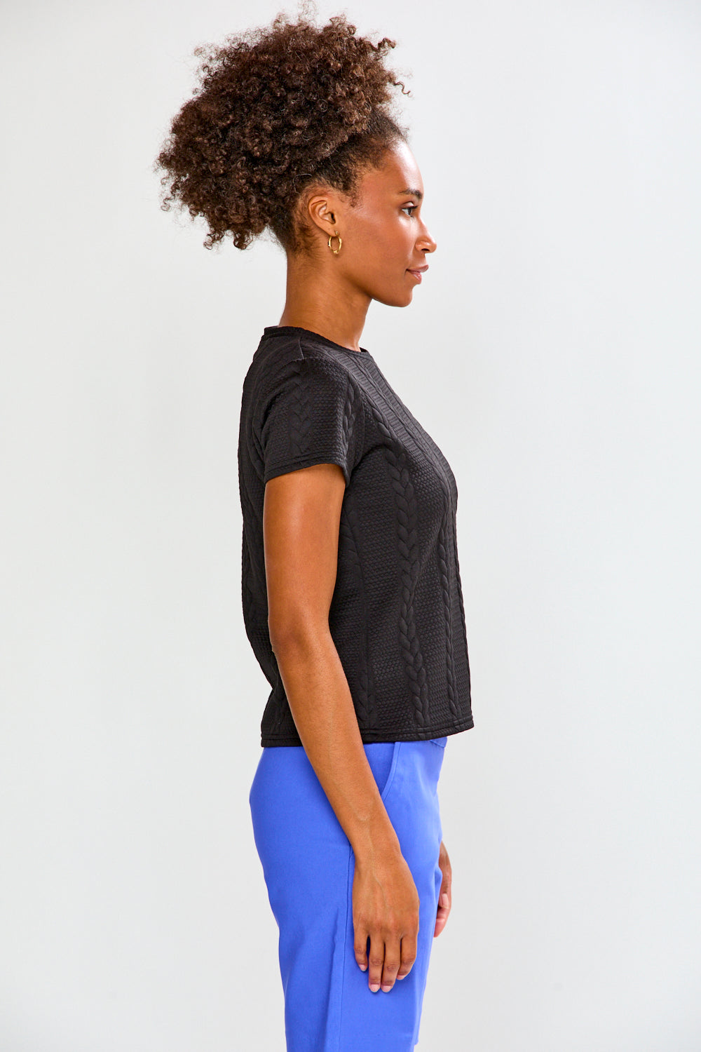 Woman wearing a black textured top and blue pants on a white background