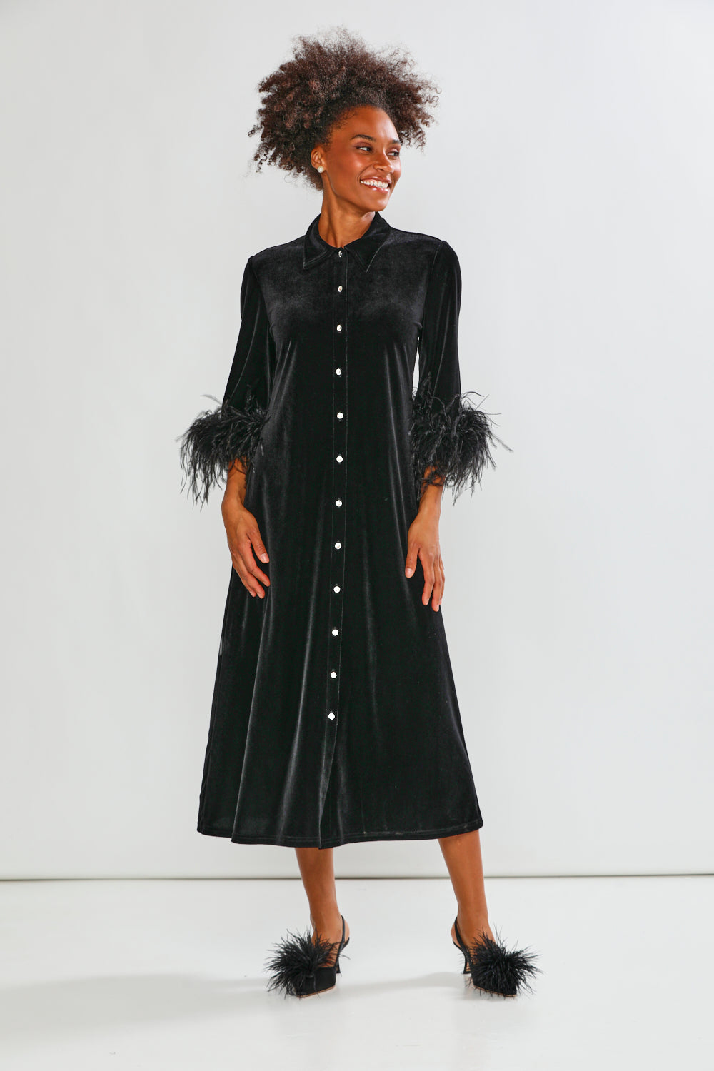 Woman wearing a black velvet dress with feathered sleeves on a white background