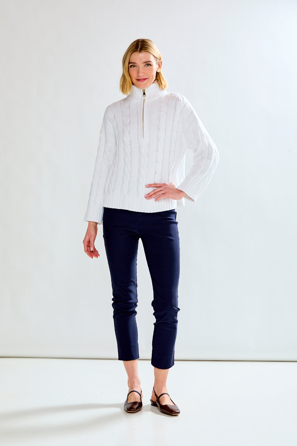 Woman wearing a white cable knit sweater against a plain background