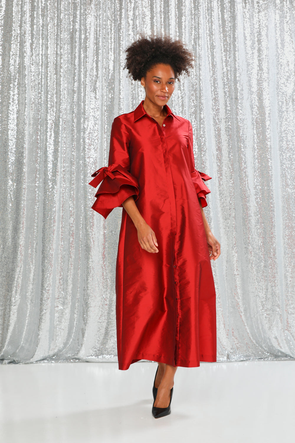 Woman wearing a red dress with ruffled sleeves against a silver curtain background