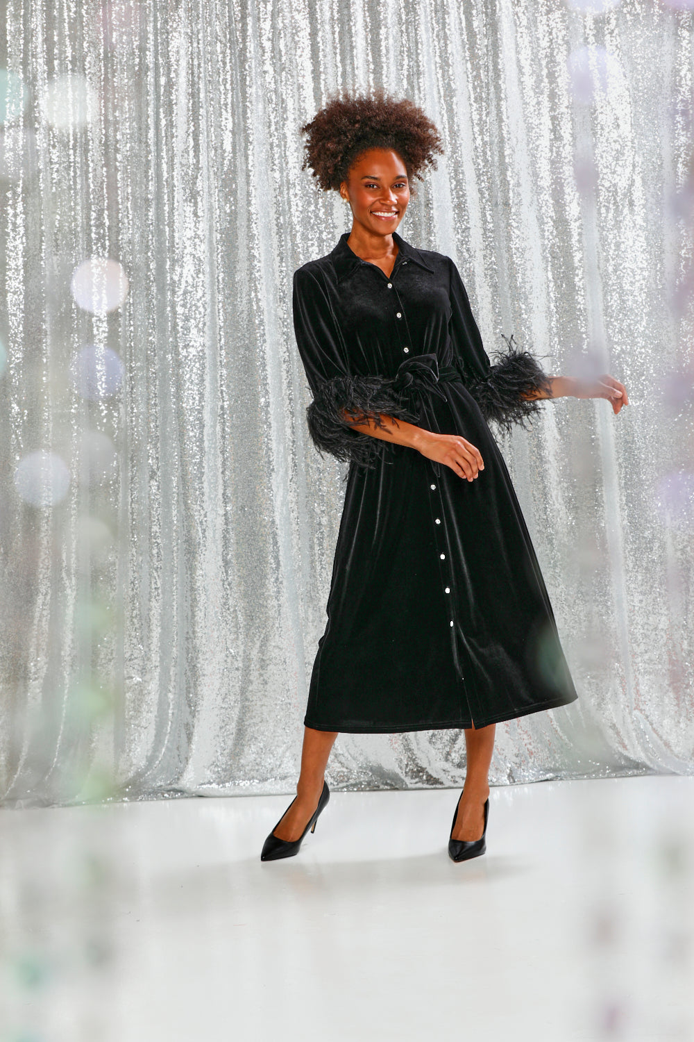 Woman wearing a black velvet dress with feathered sleeves on a white background