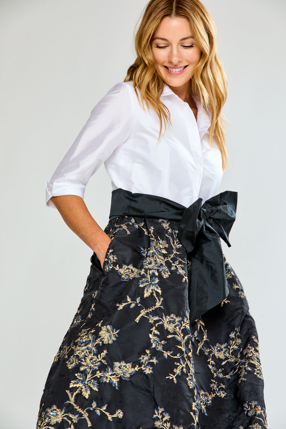 Woman wearing a dress with a white blouse and black floral skirt with a large bow on a white background