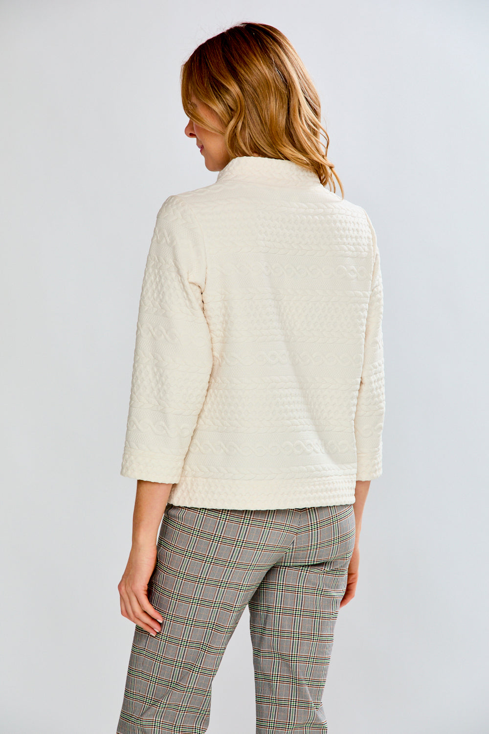 Woman wearing a cream sweater and plaid pants against a white background
