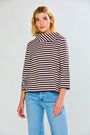 A woman modeling a brown and white horizontally striped knit top with a wide mock neck and three-quarter sleeves, paired with light blue jeans, against a light gray studio background.