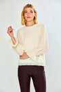 A woman modeling a cream-colored long-sleeve blouse with dramatic gathered sleeves and dark brown trousers, set against a plain light gray studio background.
