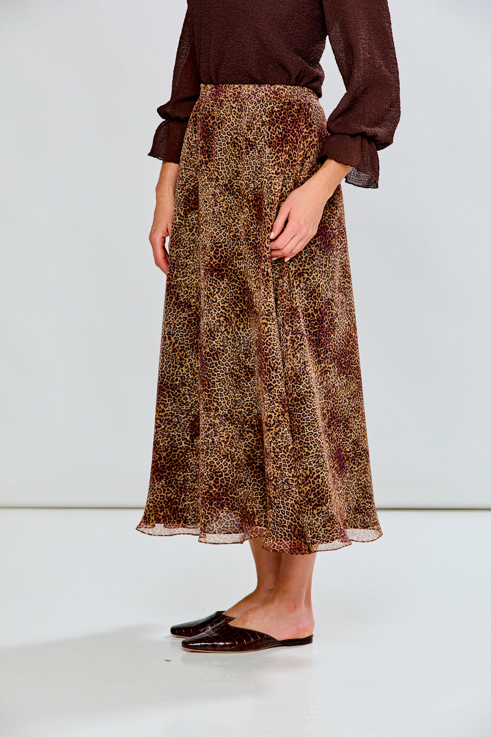 Person wearing a patterned skirt and brown top on a white background