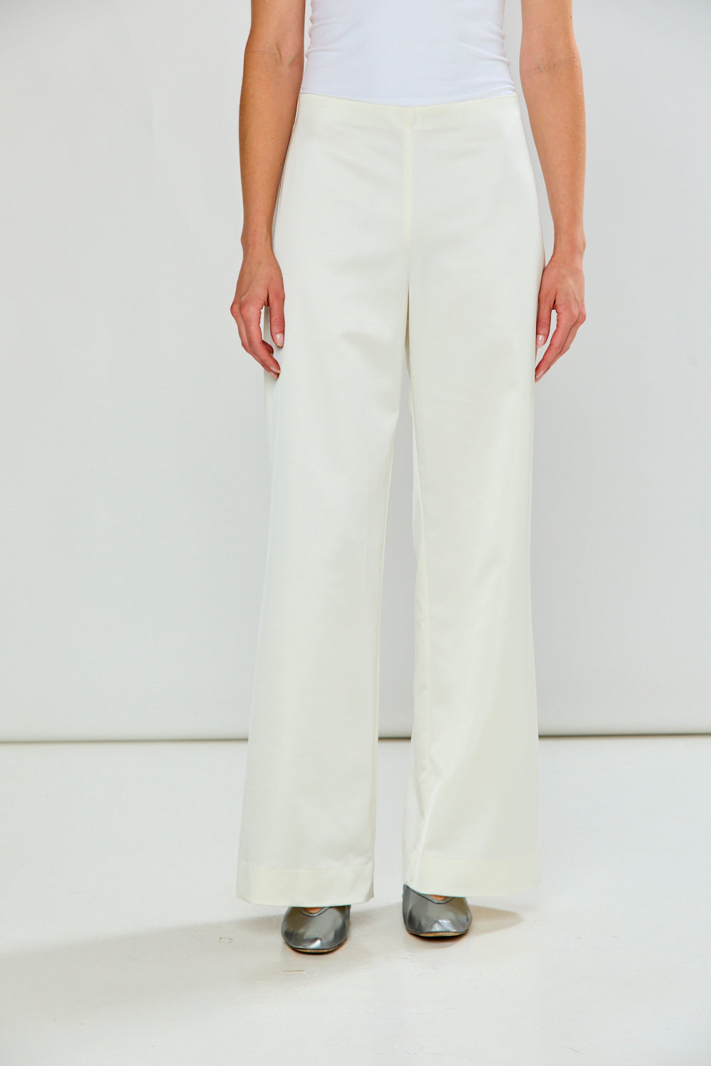 The Reyna Pant - Off White, wide leg women's pants modeled with a fitted white top and metallic pointed toe shoes in a minimalist studio setting