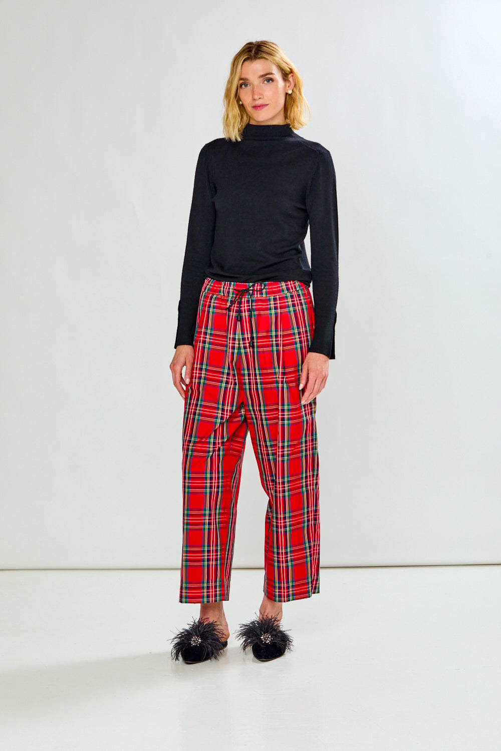The Marcia Pant - Red Plaid shown as red plaid women's pants with a high waist and cropped straight legs styled with a black top and feathered shoes.