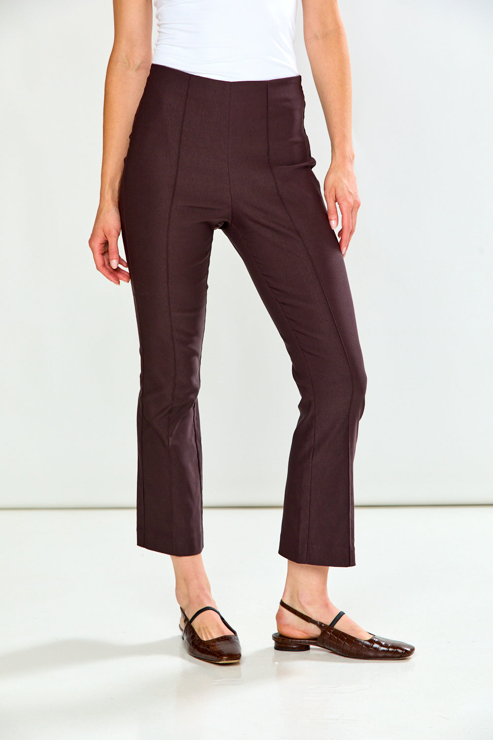 A model wearing dark brown cropped trousers, a white top, and dark brown flat shoes, shown from the waist down against a plain white studio background.