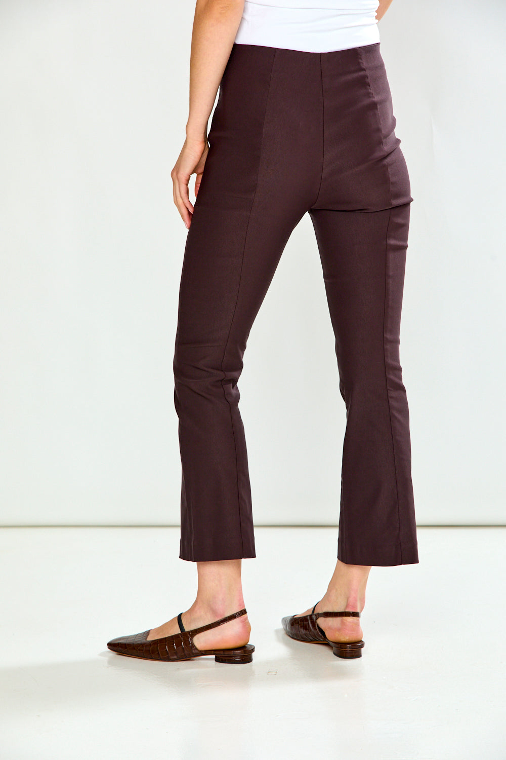 A person shown from the waist down wearing dark brown cropped flare pants and dark flat sandals against a clean white studio background.